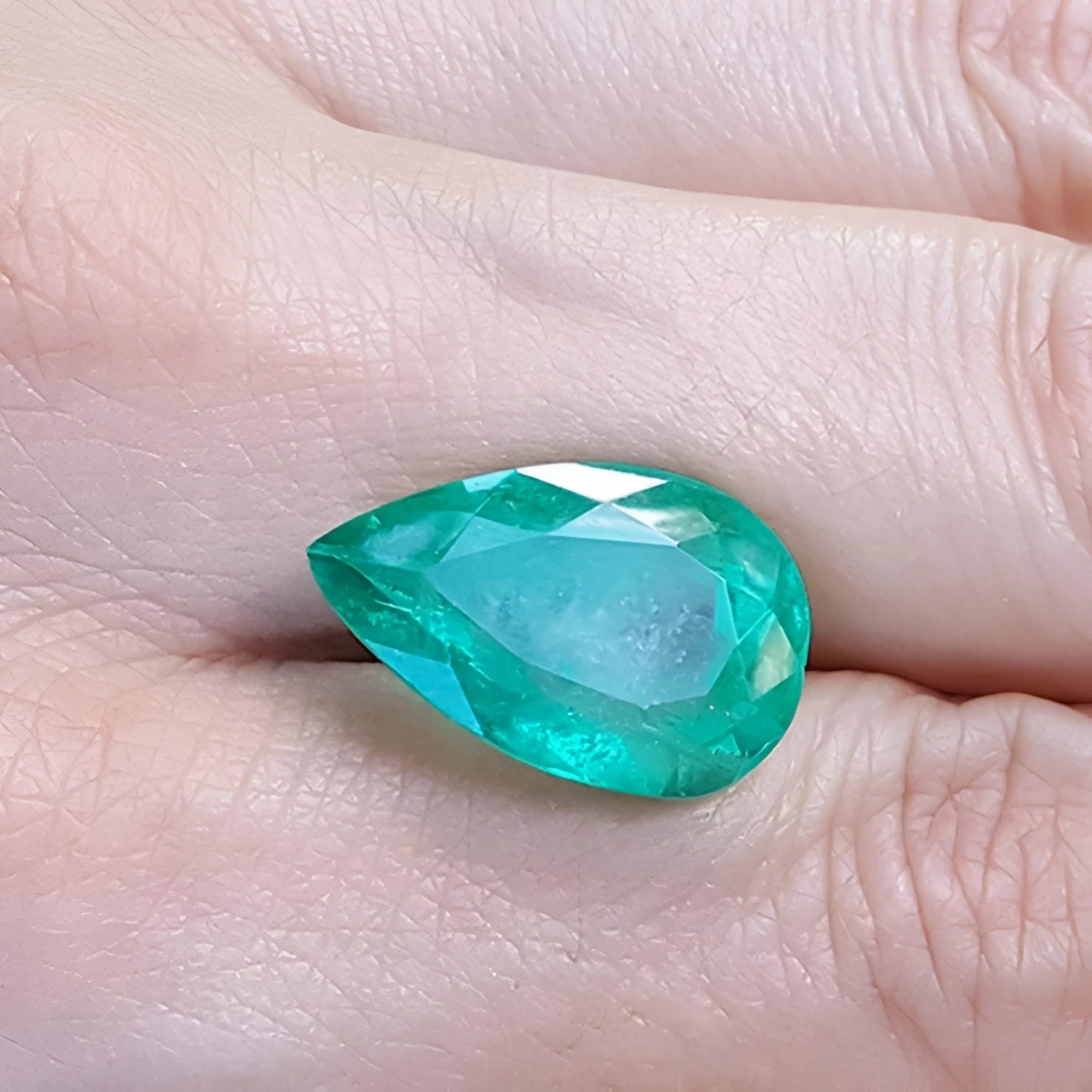 13.42 ct pear-cut Colombian loose emerald with a medium green hue, held in a hand.