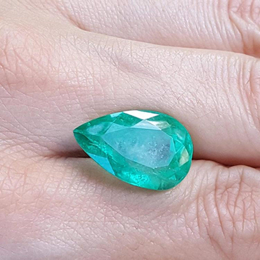 13.42 ct pear-cut Colombian loose emerald with a medium green hue, held in a hand.