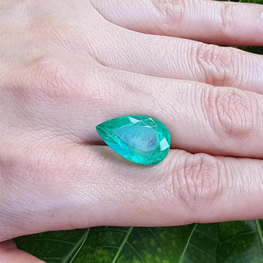 13.42 ct. pear-cut Colombian emerald, medium green, held on a hand over a green leaf.