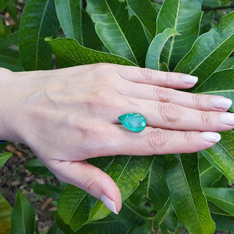 13.42 ct. pear-cut Colombian loose emerald, medium green, held on a hand against green leaves.