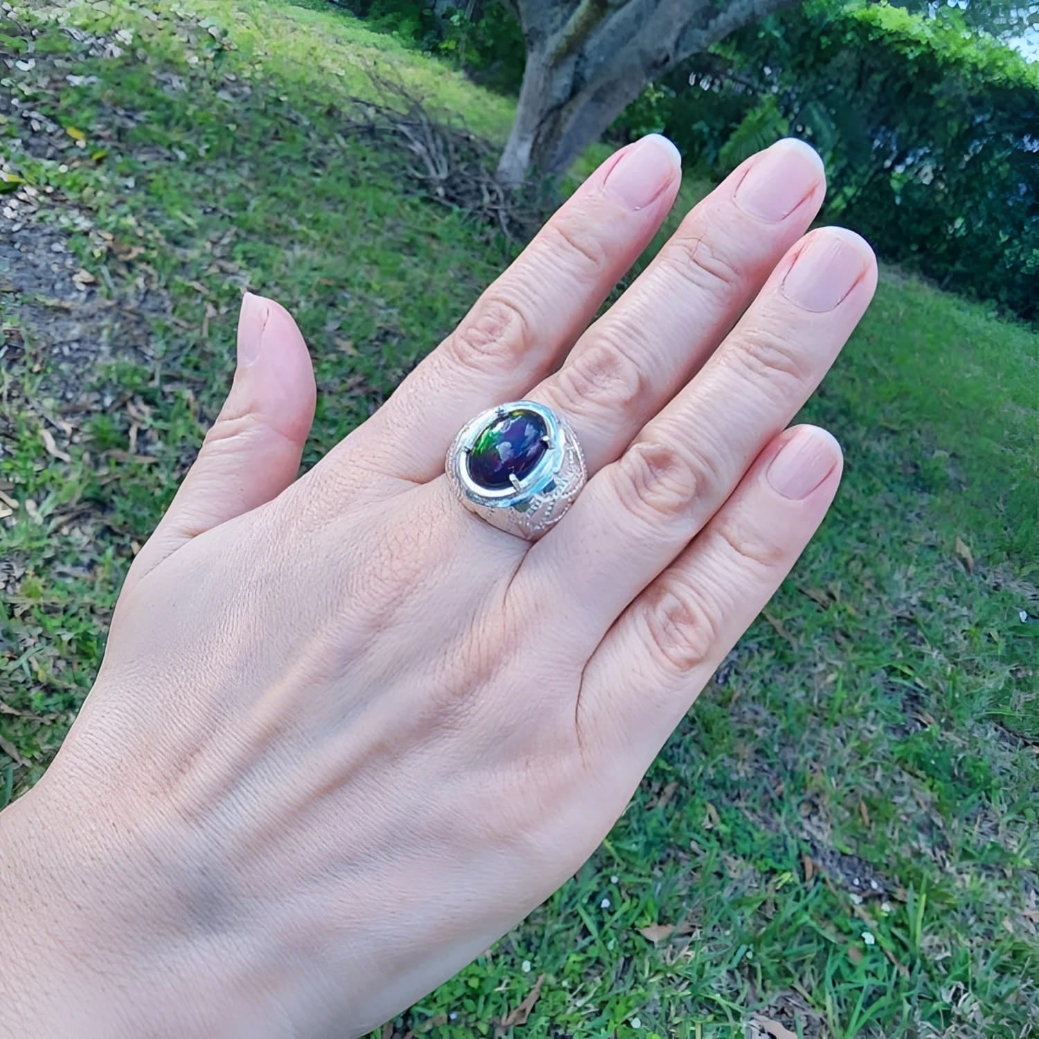 Men's black Ethiopian opal ring with red-orange and blue hues, set in sterling silver on a hand.