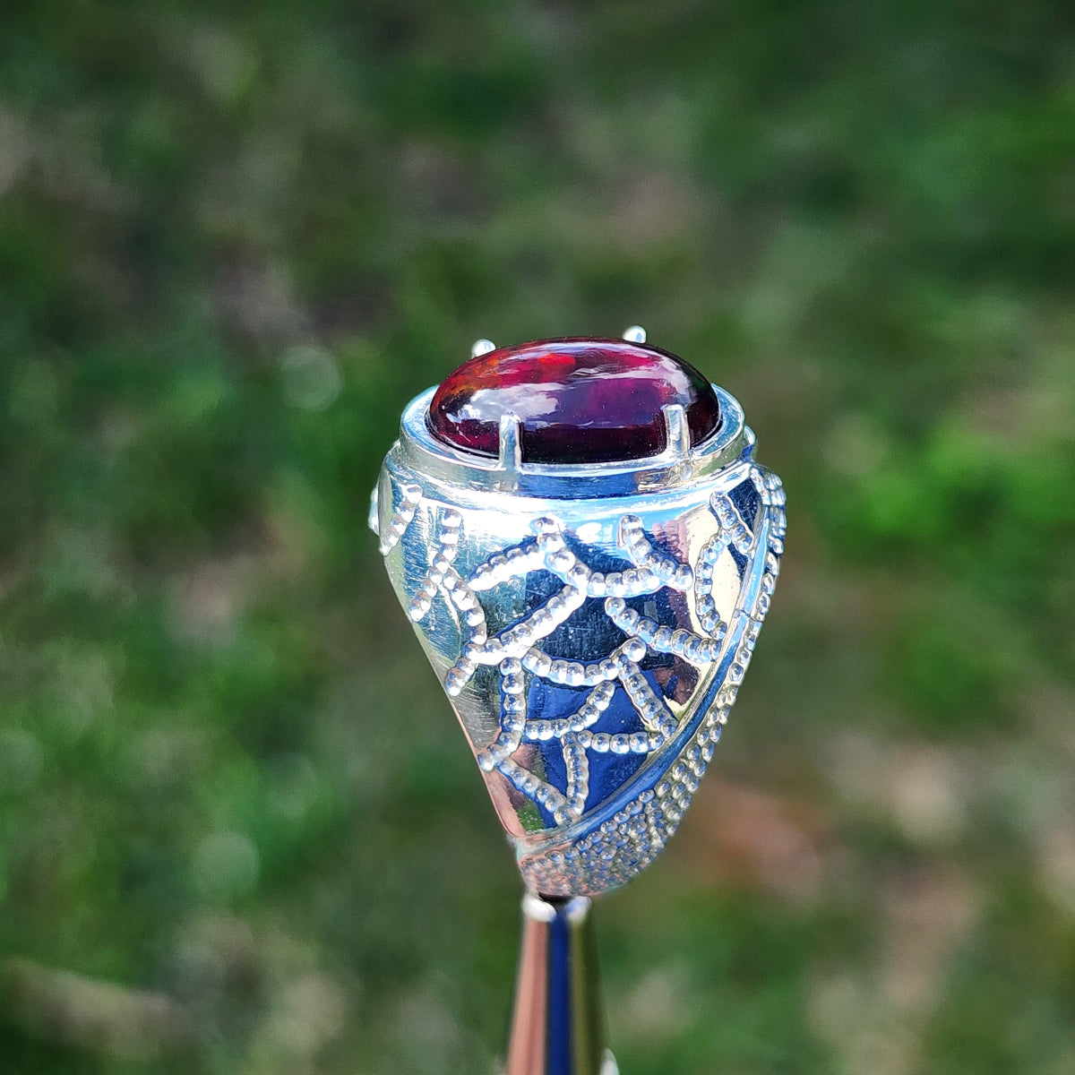 Elegant silver ring for men with a large red color Ethiopian black opal against a blurred green background