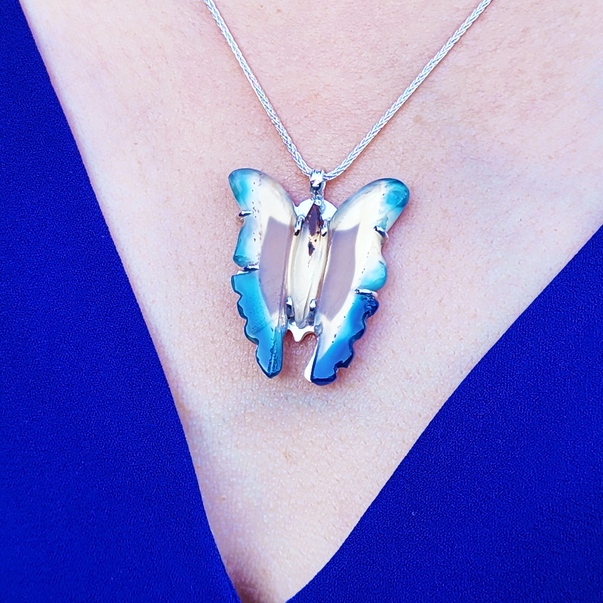 Butterfly-shaped pendant necklace on a person&#39;s neck against a blue background