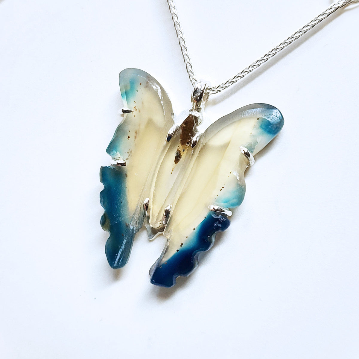 Butterfly-shaped pendant with blue and beige wings on a white background