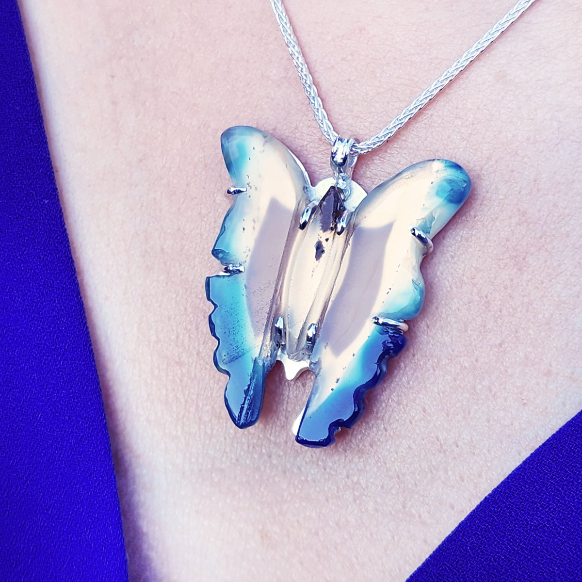Butterfly-shaped pendant on a chain against a blue and white background