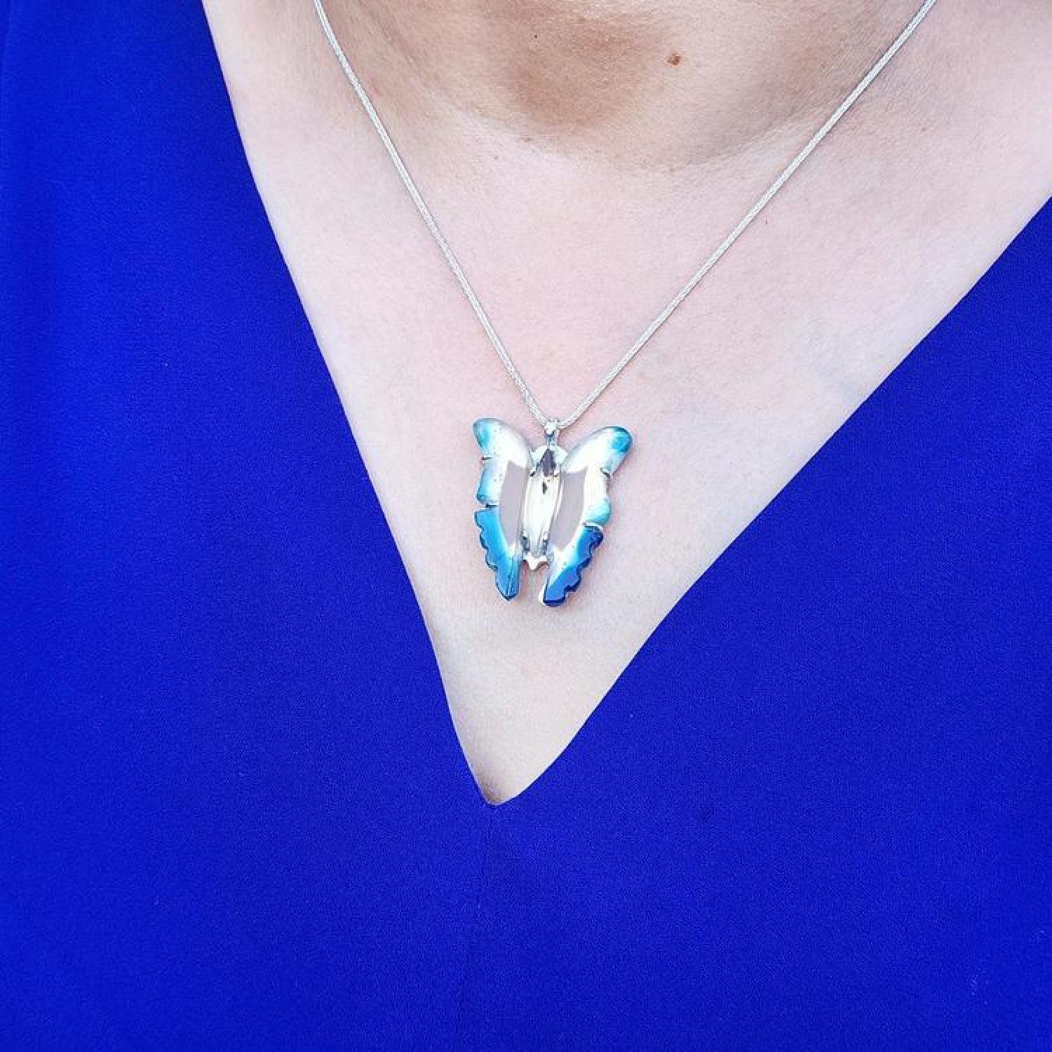 Blue agate butterfly pendant necklace with sterling silver chain on a person wearing a blue top.