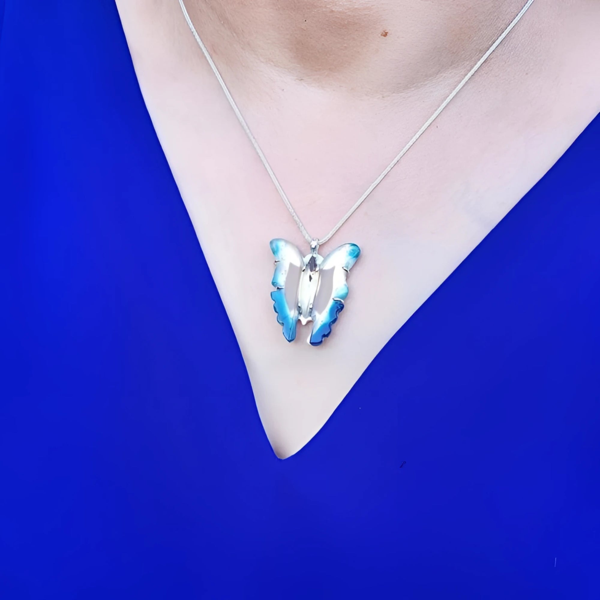 Blue agate butterfly pendant necklace with sterling silver chain on a person wearing a blue top.