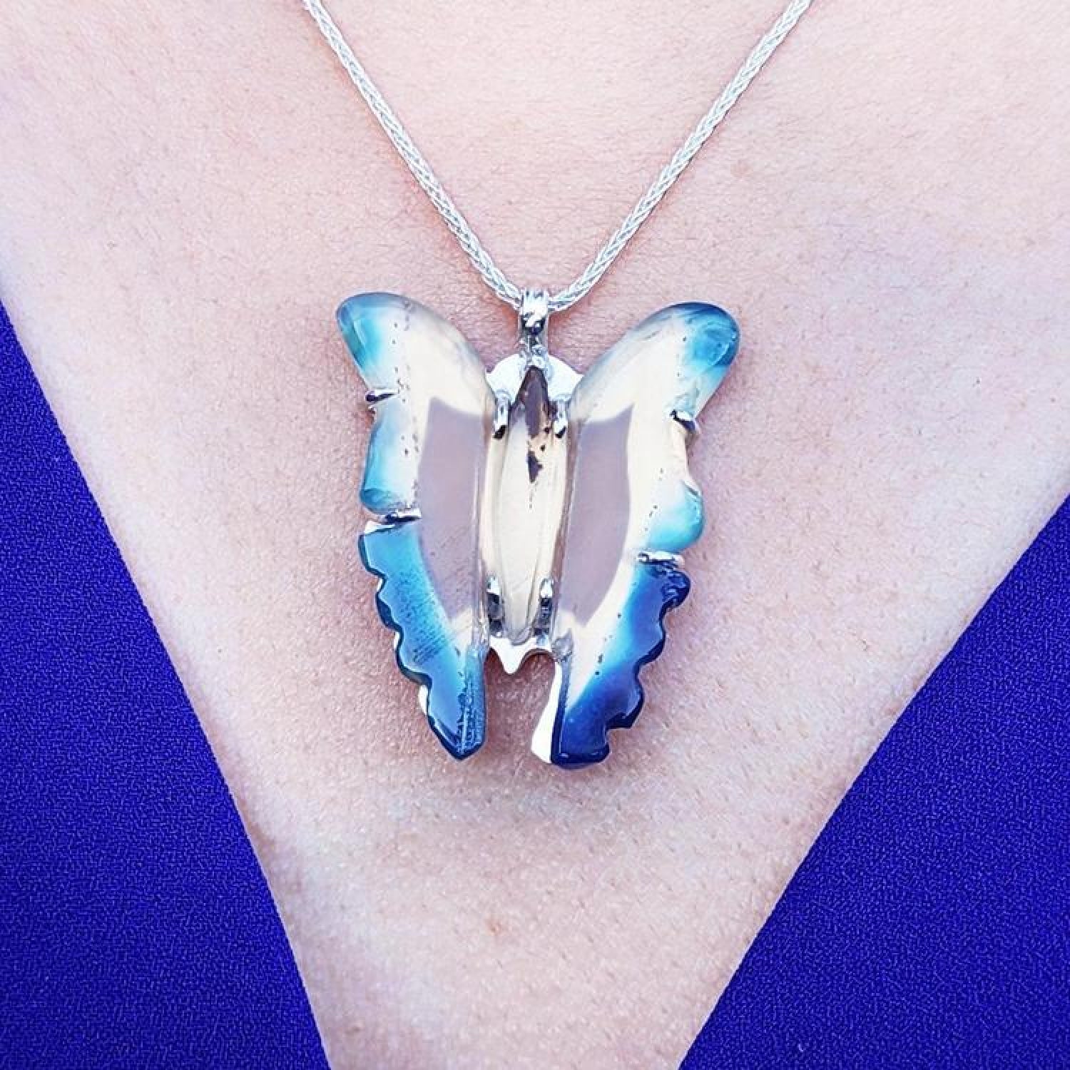 Natural blue agate butterfly pendant with sterling silver frame on a silver chain, worn on a blue top.