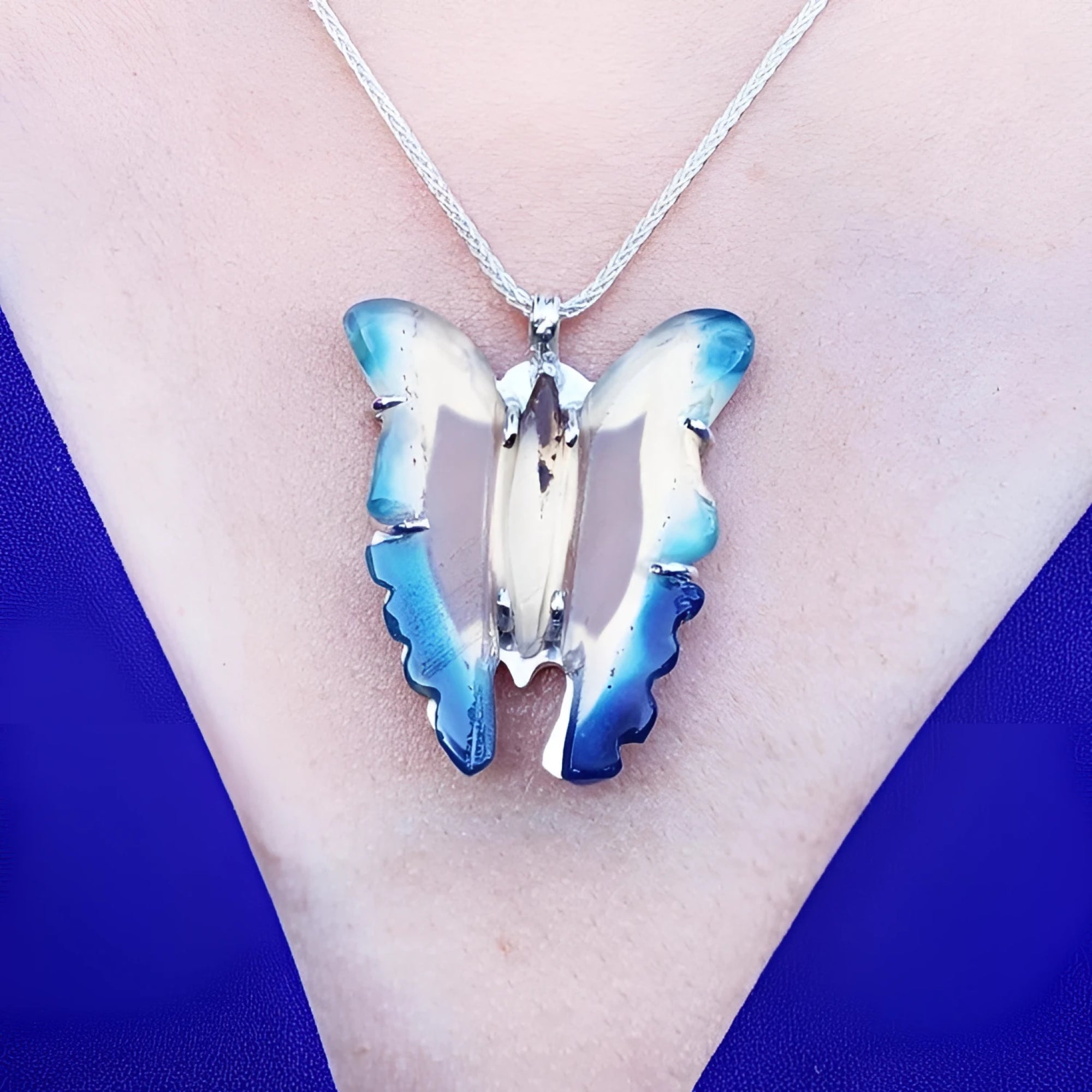 Natural blue agate butterfly pendant with sterling silver frame on a silver chain, worn on a blue top.