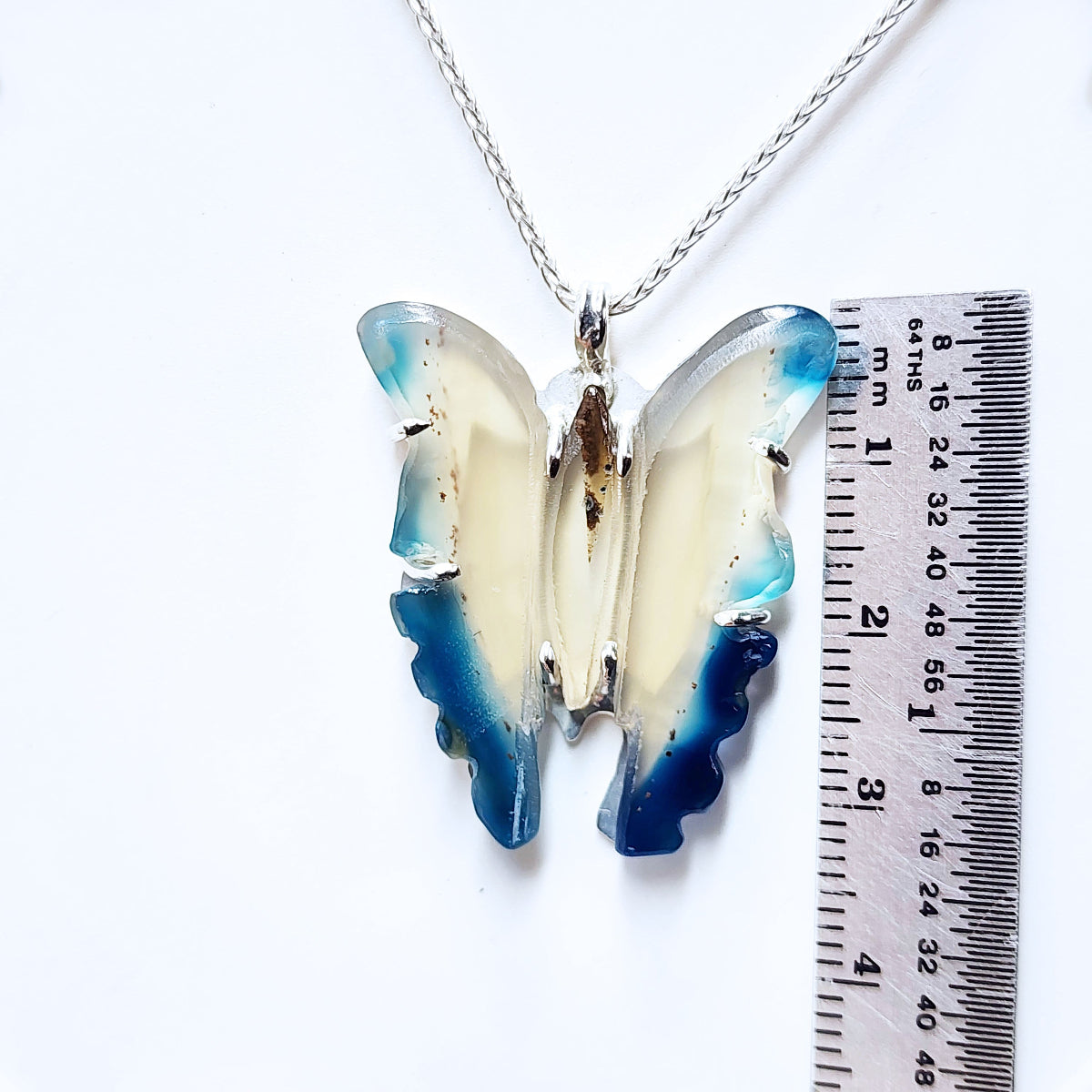 Butterfly-shaped pendant on a chain with a ruler for scale on a white background