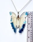 Butterfly-shaped pendant on a chain with a ruler for scale on a white background