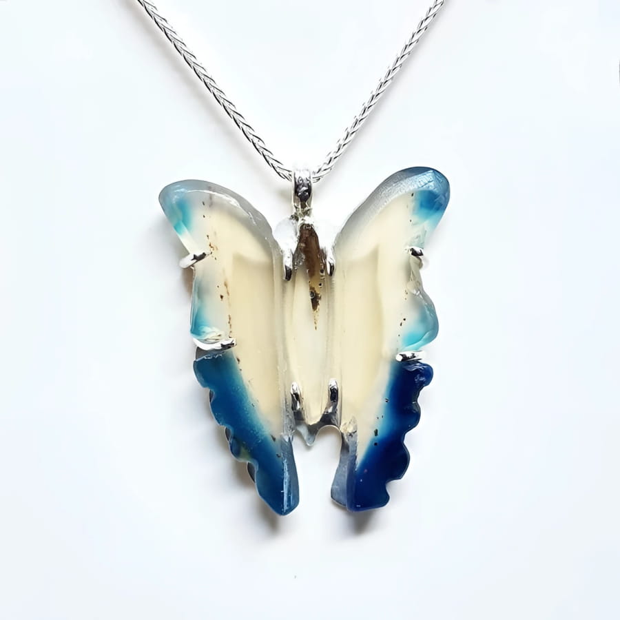 Hand-carved blue agate butterfly pendant with cream body and blue wings, set in sterling silver.