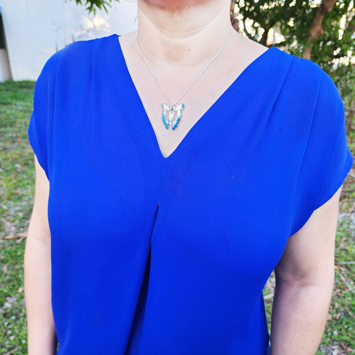 Person wearing a blue top with a necklace featuring a turquoise pendant outdoors.