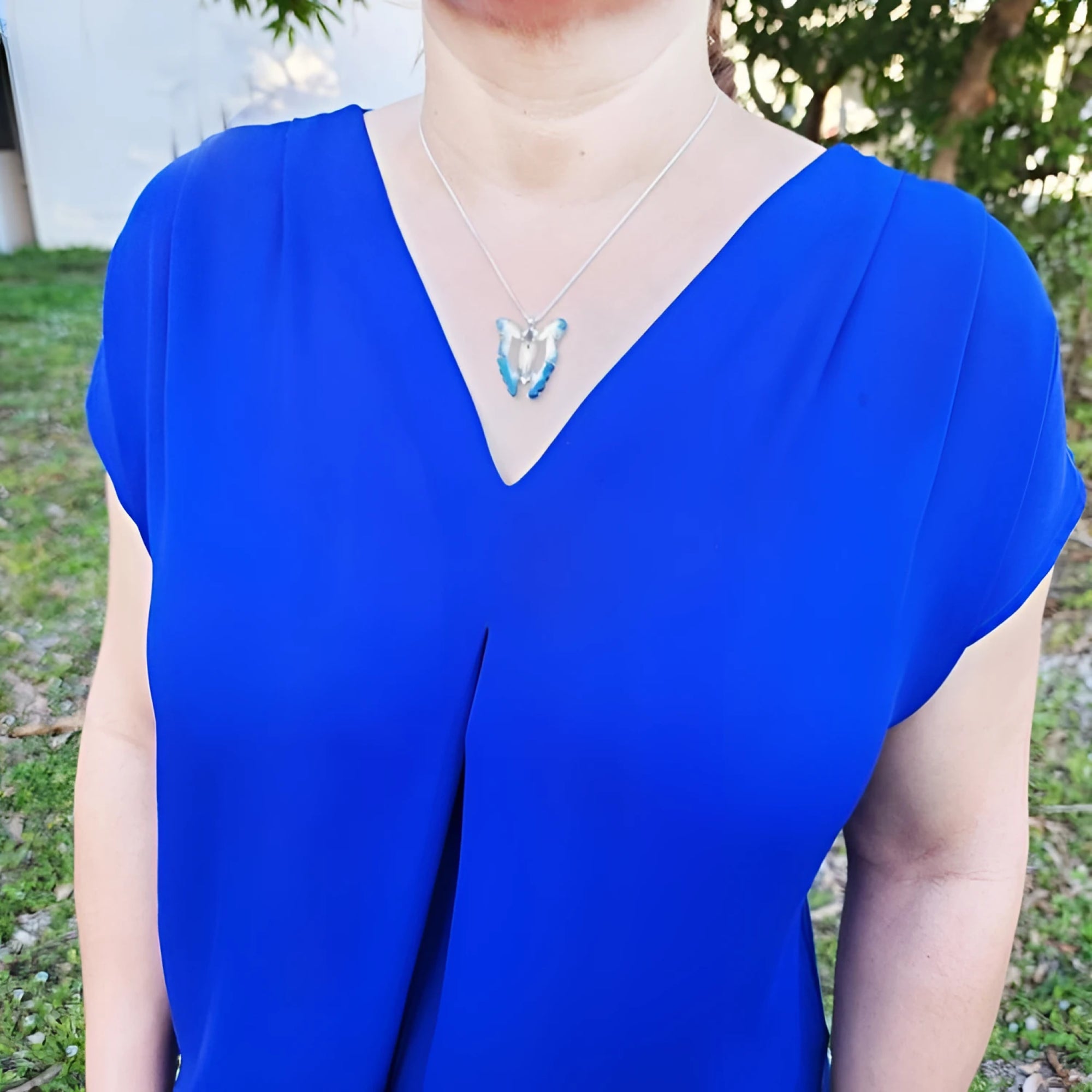 Natural blue agate butterfly pendant necklace with sterling silver frame on a woman's blue top.