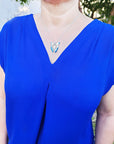 Person wearing a blue top with a necklace featuring a turquoise pendant outdoors.