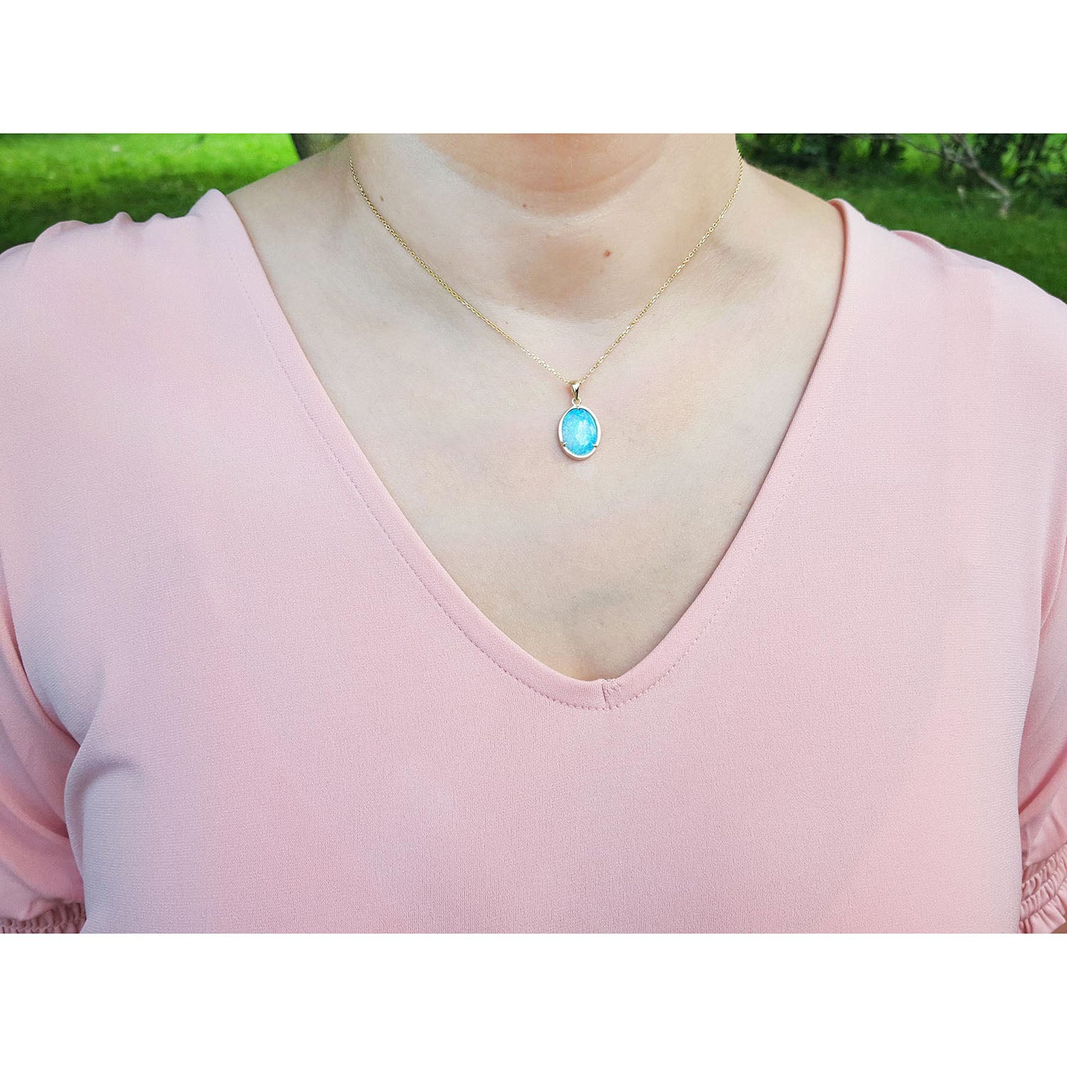 Person wearing a pink top with a necklace featuring a blue opal pendant outdoors.