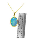 Opal pendant necklace with gold chain next to a ruler for scale on a white background