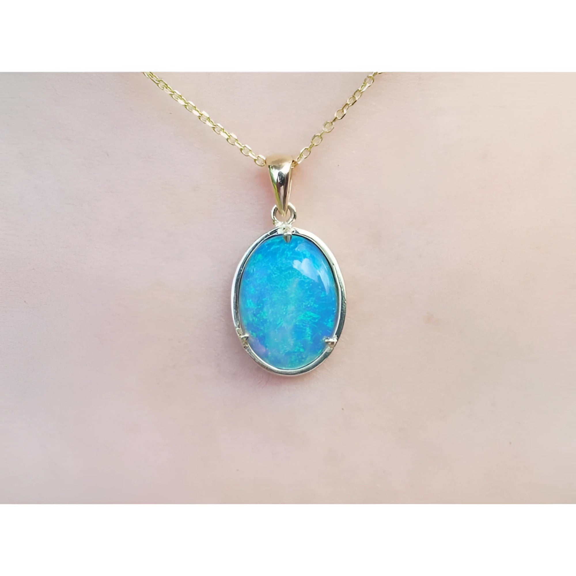 Oval blue-green opal pendant in 14K yellow gold on a delicate chain, worn on skin.
