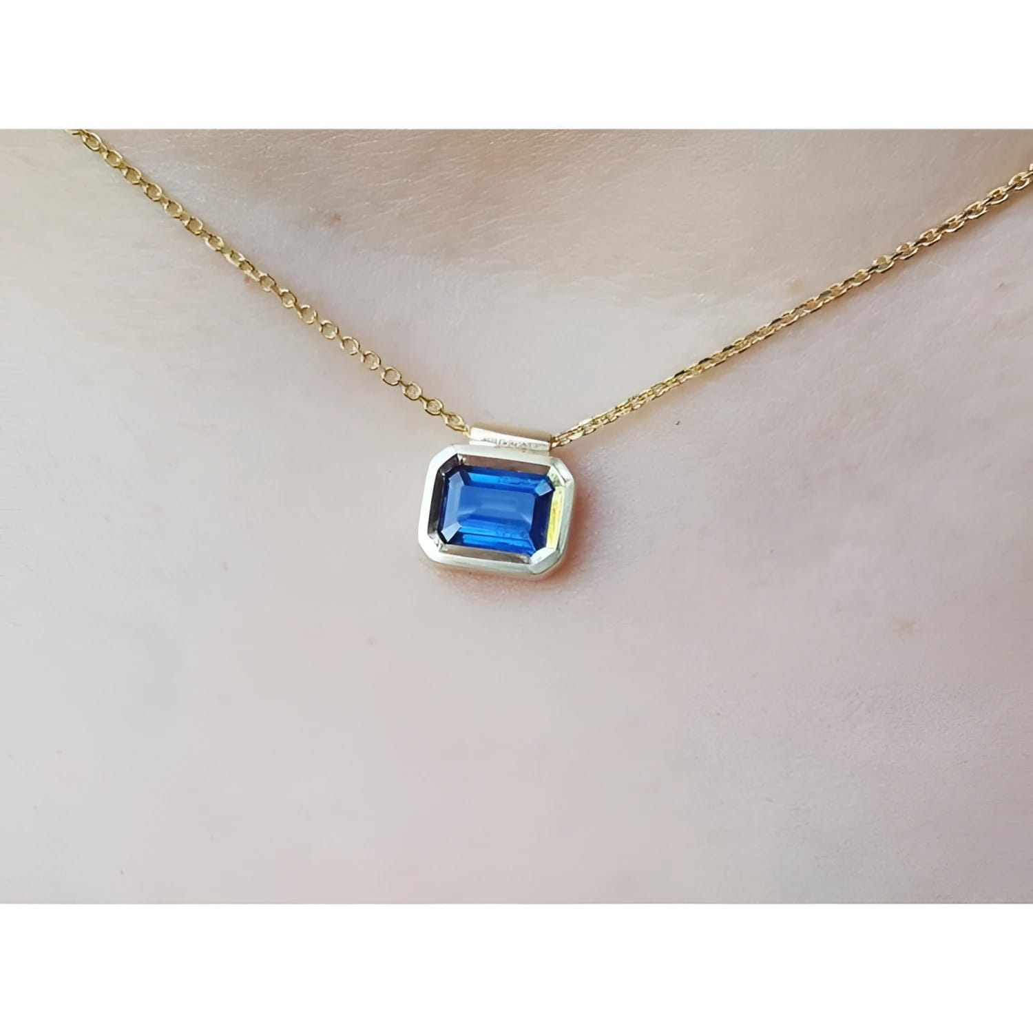 Gold necklace with a blue natural sapphire gemstone bezel set pendant on a woman's neck