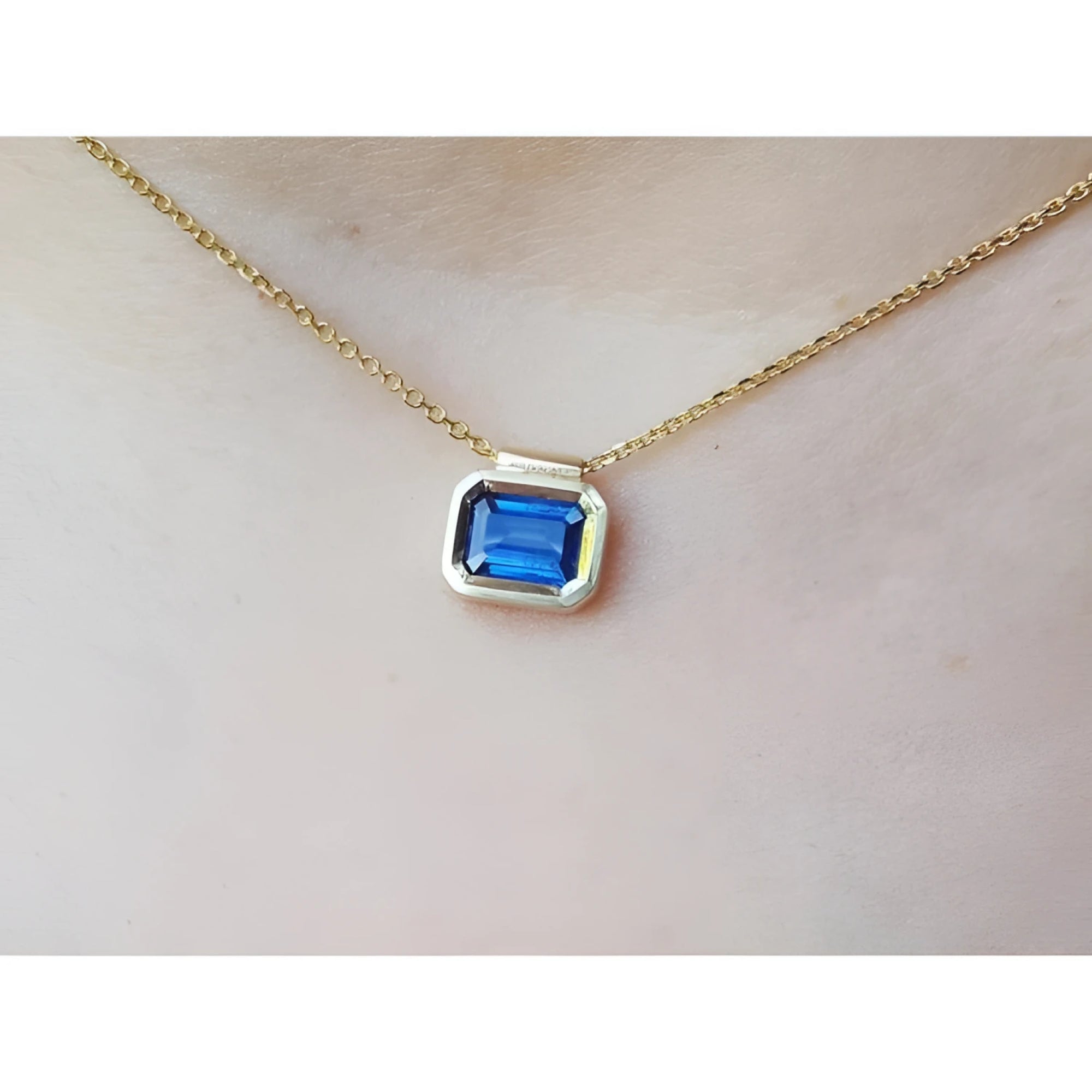 Gold necklace with a blue natural sapphire gemstone bezel set pendant on a woman's neck