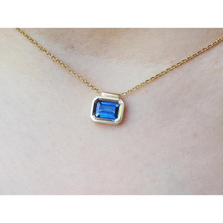 Gold necklace with a blue natural sapphire gemstone bezel set pendant on a woman's neck