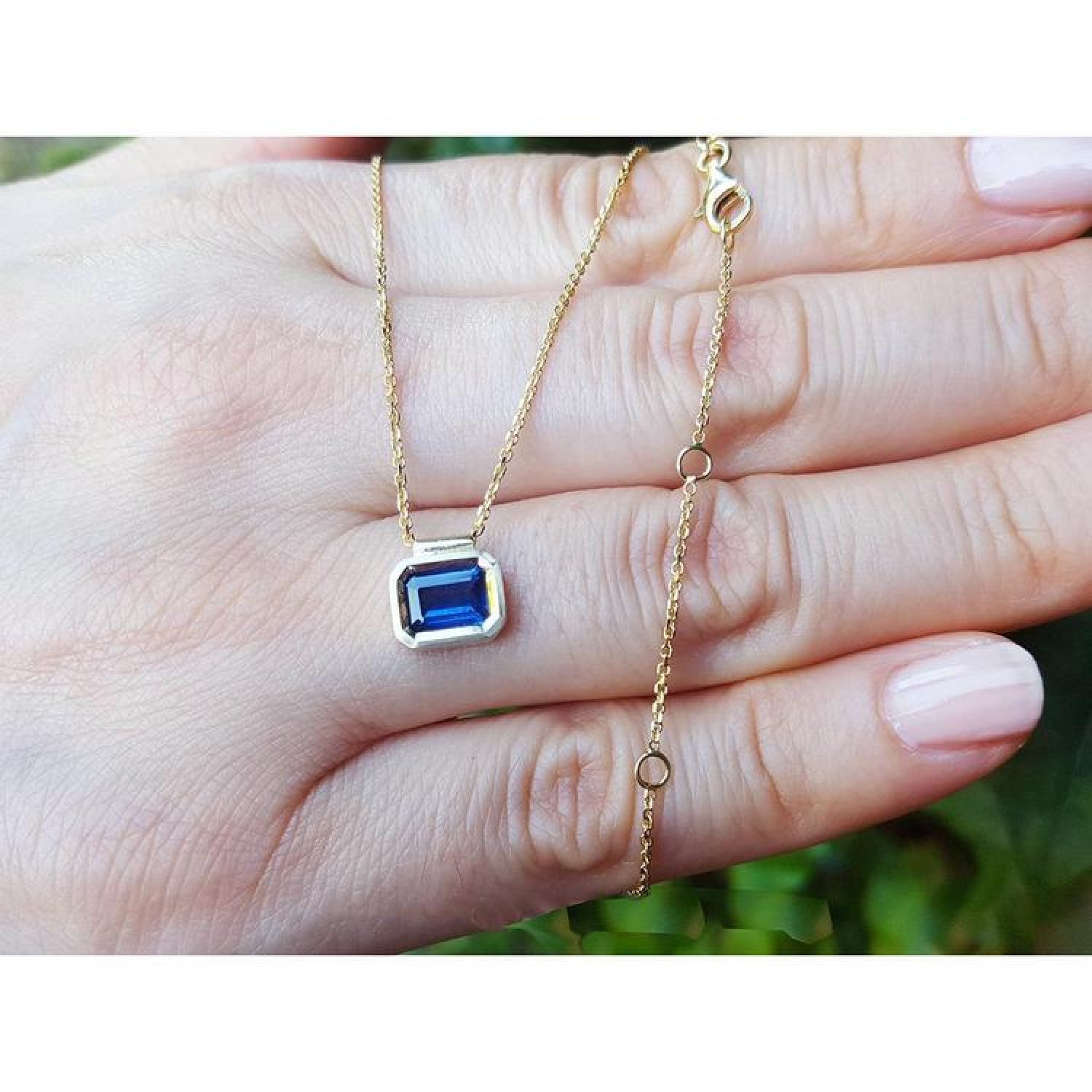 1.01 ct blue sapphire choker necklace, bezel set in 14K gold, on a hand.