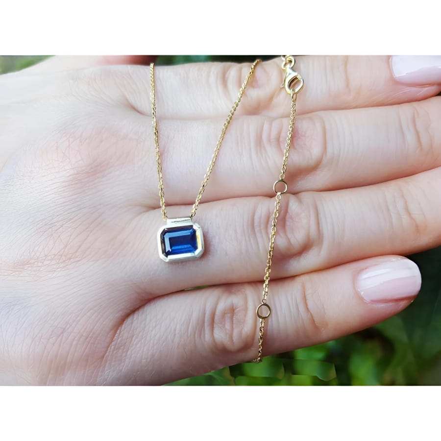 1.01 ct blue sapphire choker necklace, bezel set in 14K gold, on a hand.