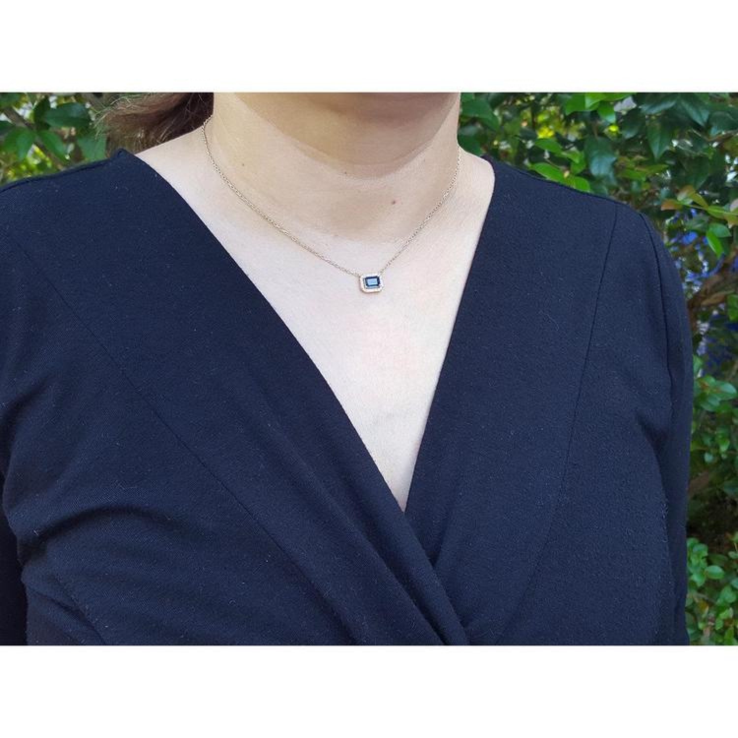 Woman wearing a 14K yellow gold necklace with an east-west emerald cut blue sapphire and diamond pendant.