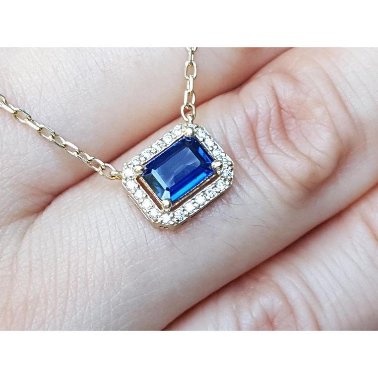 Displaying on fingers top view of a blue sapphire necklace emerald cut halo diamonds in 14k yellow gold.