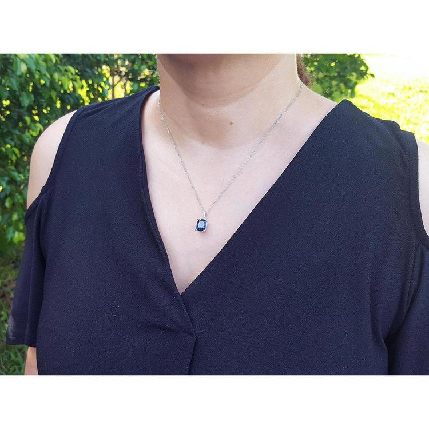 Woman wearing a 4.11 ct cushion cut deep blue sapphire solitaire pendant on a 14K white gold chain.