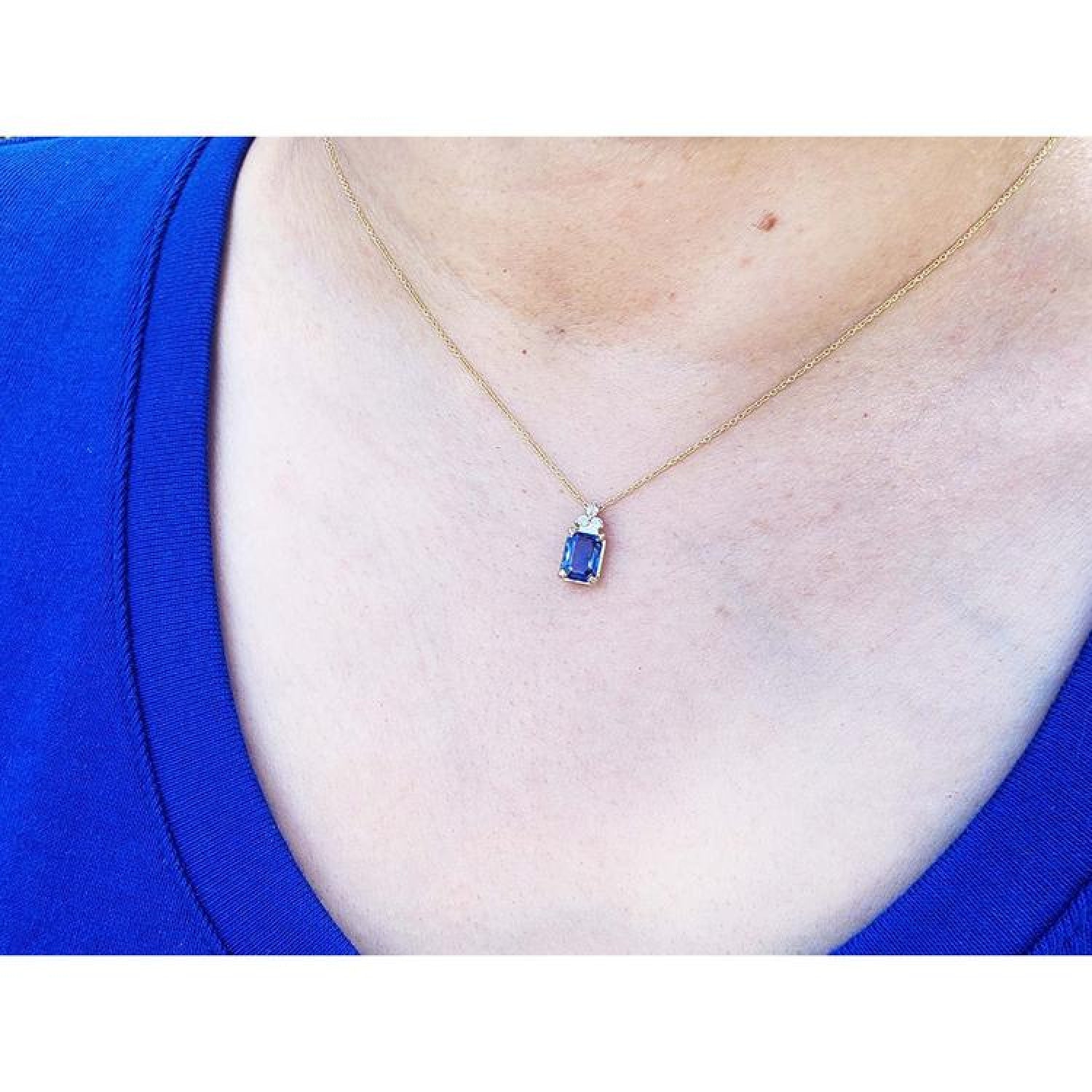 14k gold necklace with a rectangular blue sapphire pendant and three accent diamonds on a person's neck.