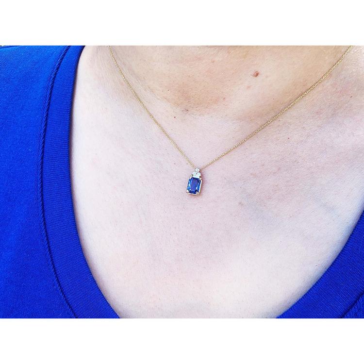 Gold necklace with a blue natural sapphire pendant worn by a person in a blue shirt.