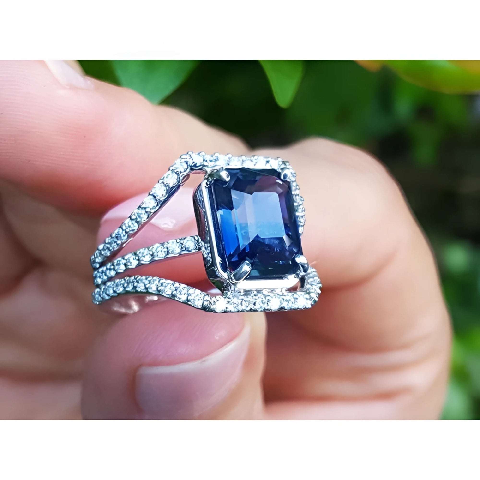 18K gold ring with a 4.51 ct emerald-cut blue sapphire and a three-row diamond band.