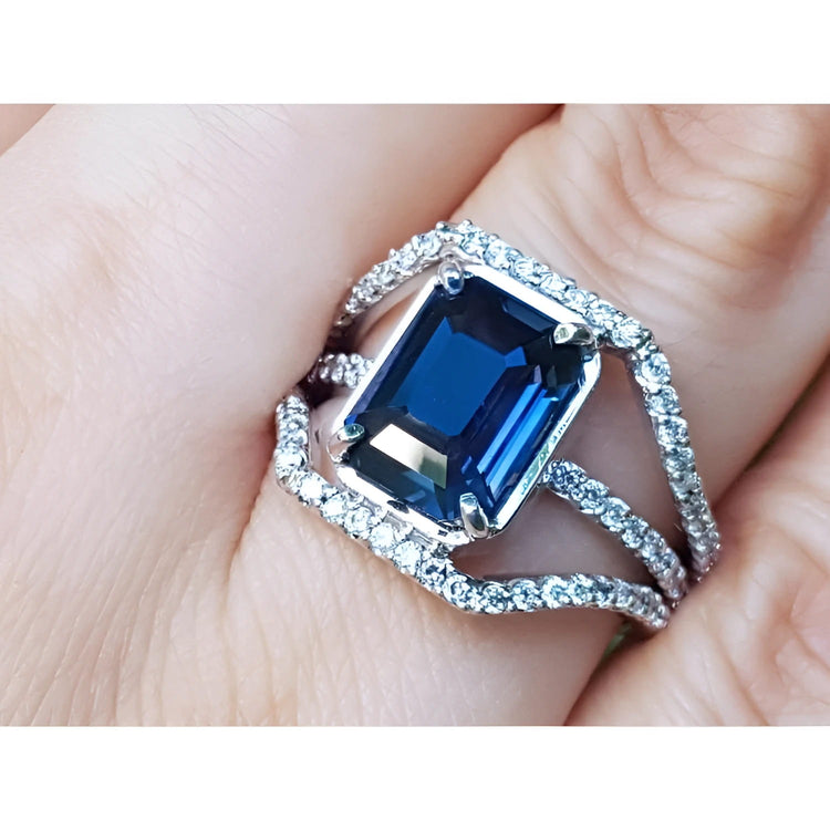 18k white gold ring with a natural blue sapphire certified gemstone untreated in an emerald cut ,held on a finger.