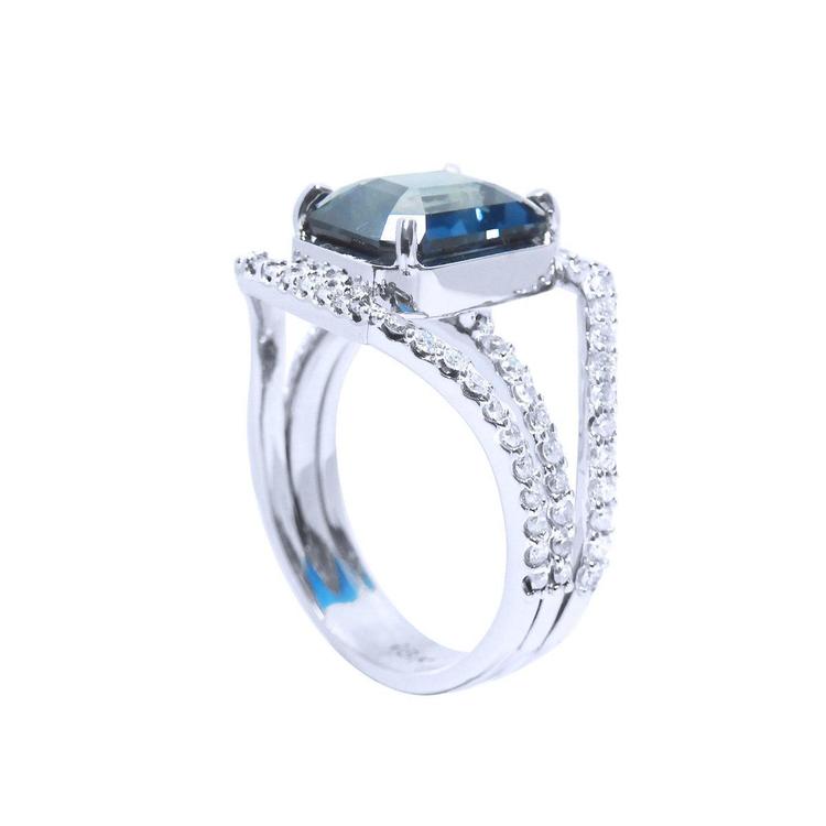 18K white gold ring with a 4.51 ct emerald-cut blue sapphire and a three-row diamond band.