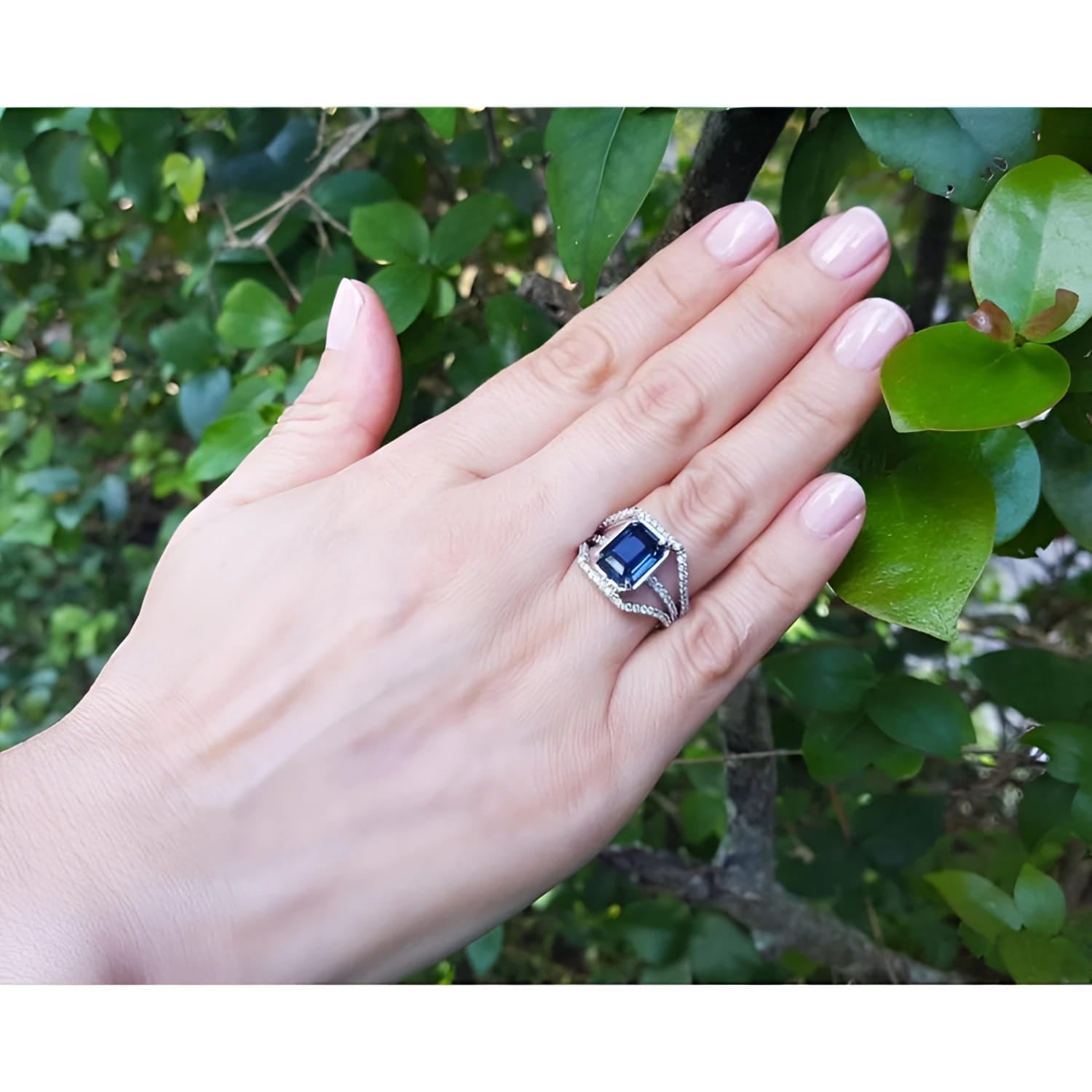 Women's 18K gold ring with a 4.51 ct emerald cut blue sapphire and three-row diamond band on a hand.