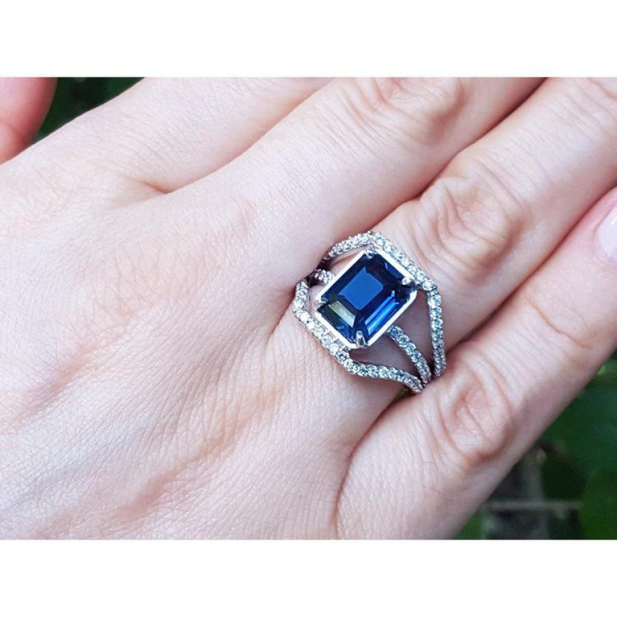 18K gold ring with a 4.51 ct emerald cut blue sapphire and a three-row diamond band.