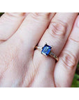 A 14k yellow gold ring with a blue natural sapphire rich medium-dark hue, flanked by two tapered baguette natural diamonds on a person's finger.