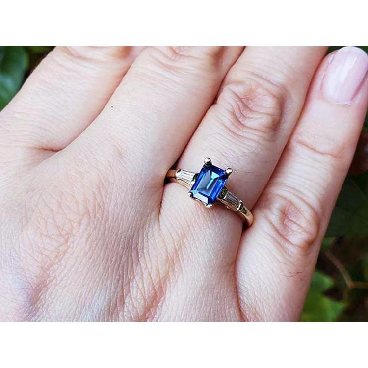 Gold ring with a blue natural sapphire on a person's finger against a natural background