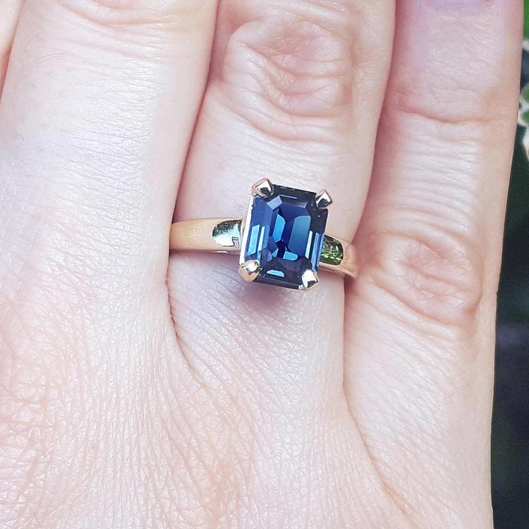 Blue sapphire solitaire ring for women emerald cut 14k yellow gold, on a person's finger