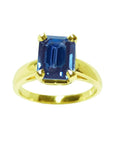 A women’s blue sapphire solitaire ring featuring a deep blue, rectangular emerald-cut sapphire set in 14k yellow gold.