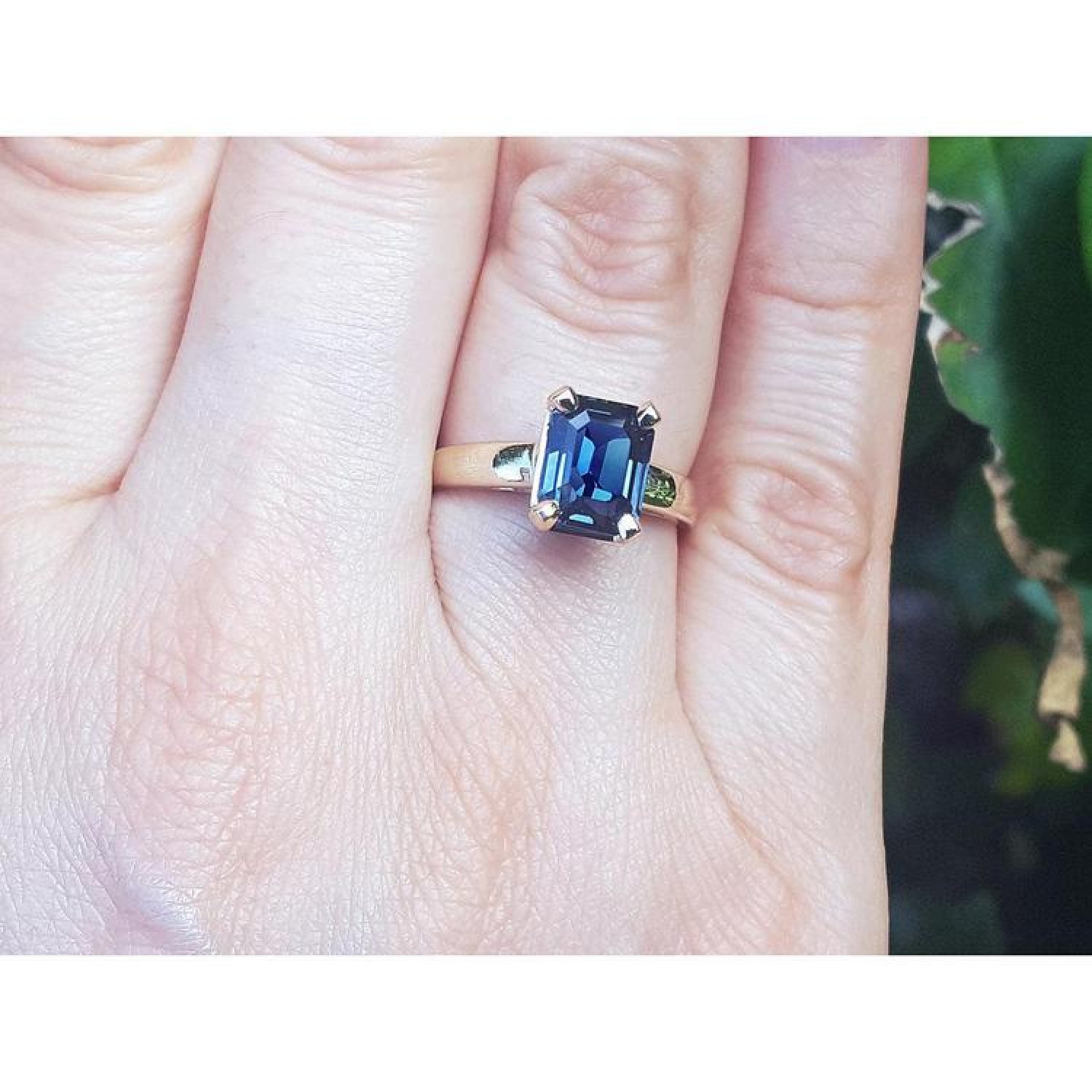 Emerald cut 3.13 ct. deep blue sapphire solitaire ring in 14K yellow gold on a hand.