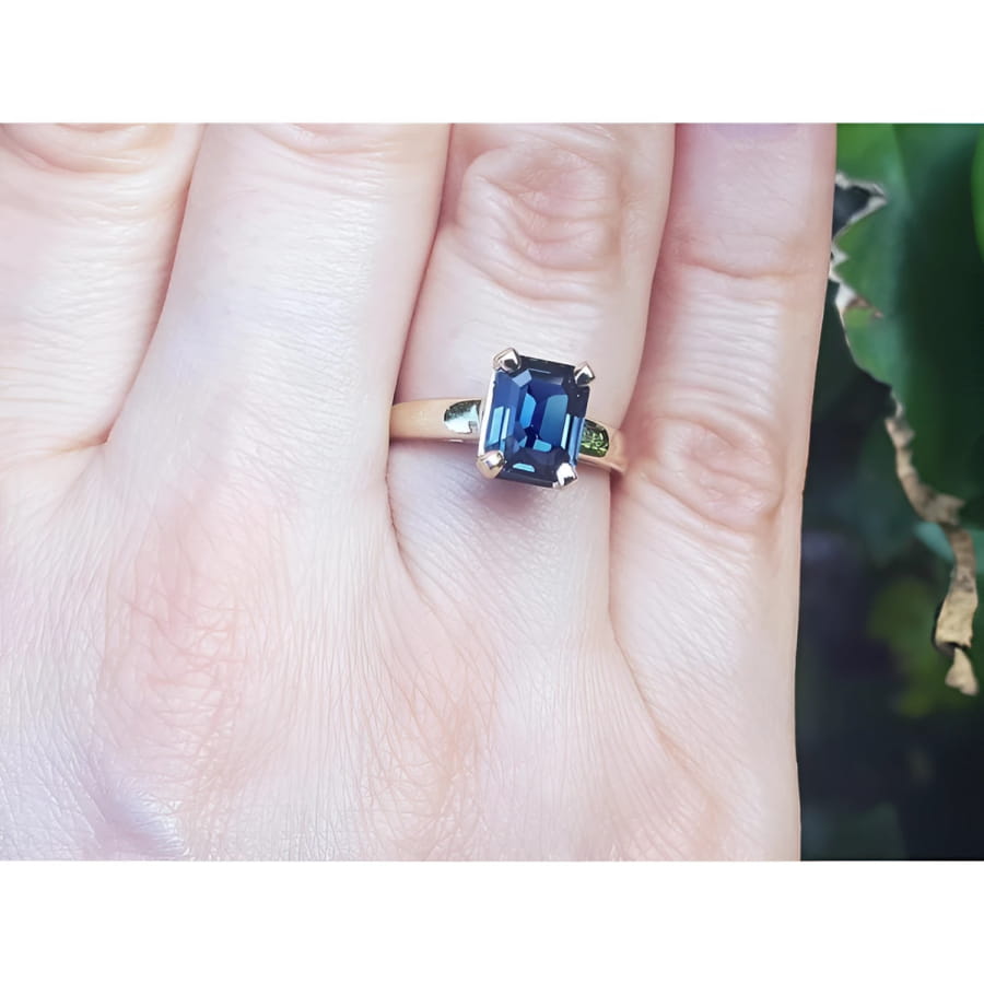 Emerald cut 3.13 ct. deep blue sapphire solitaire ring in 14K yellow gold on a hand.