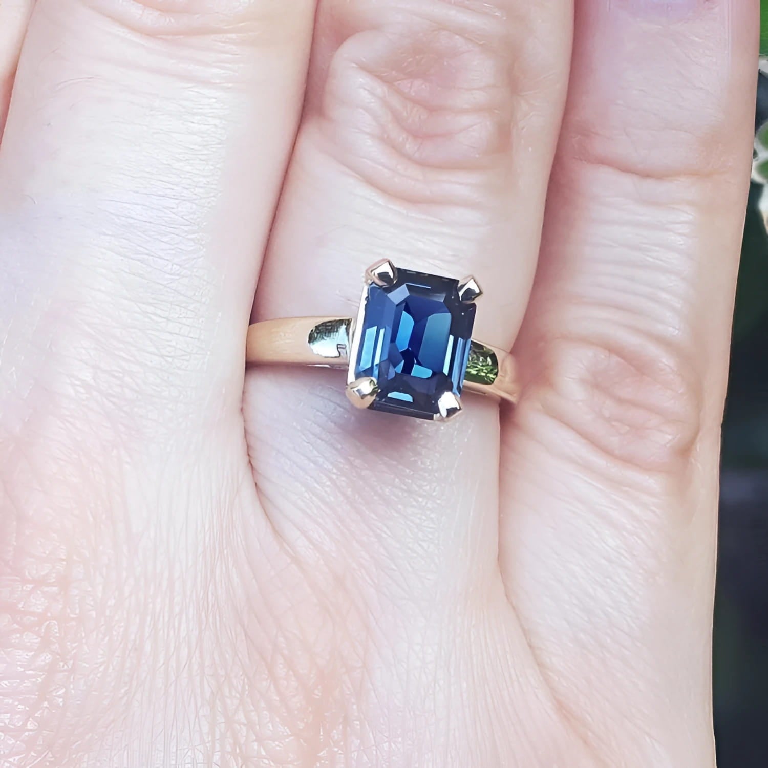 Blue sapphire solitaire ring for women emerald cut 14k yellow gold, on a person's finger.