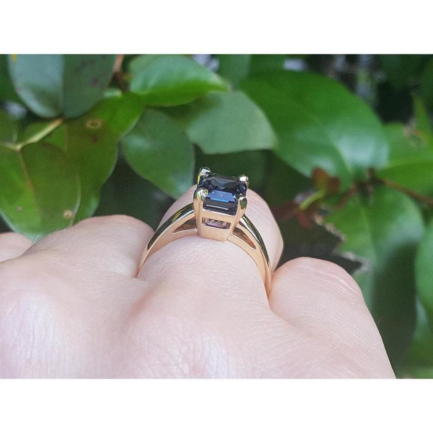 3.13 ct. emerald cut deep blue sapphire solitaire ring in 14K yellow gold on a hand.