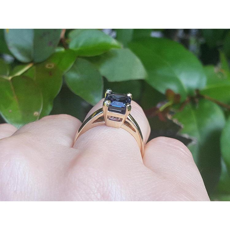 3.13 ct. emerald cut deep blue sapphire solitaire ring in 14K yellow gold on a hand.