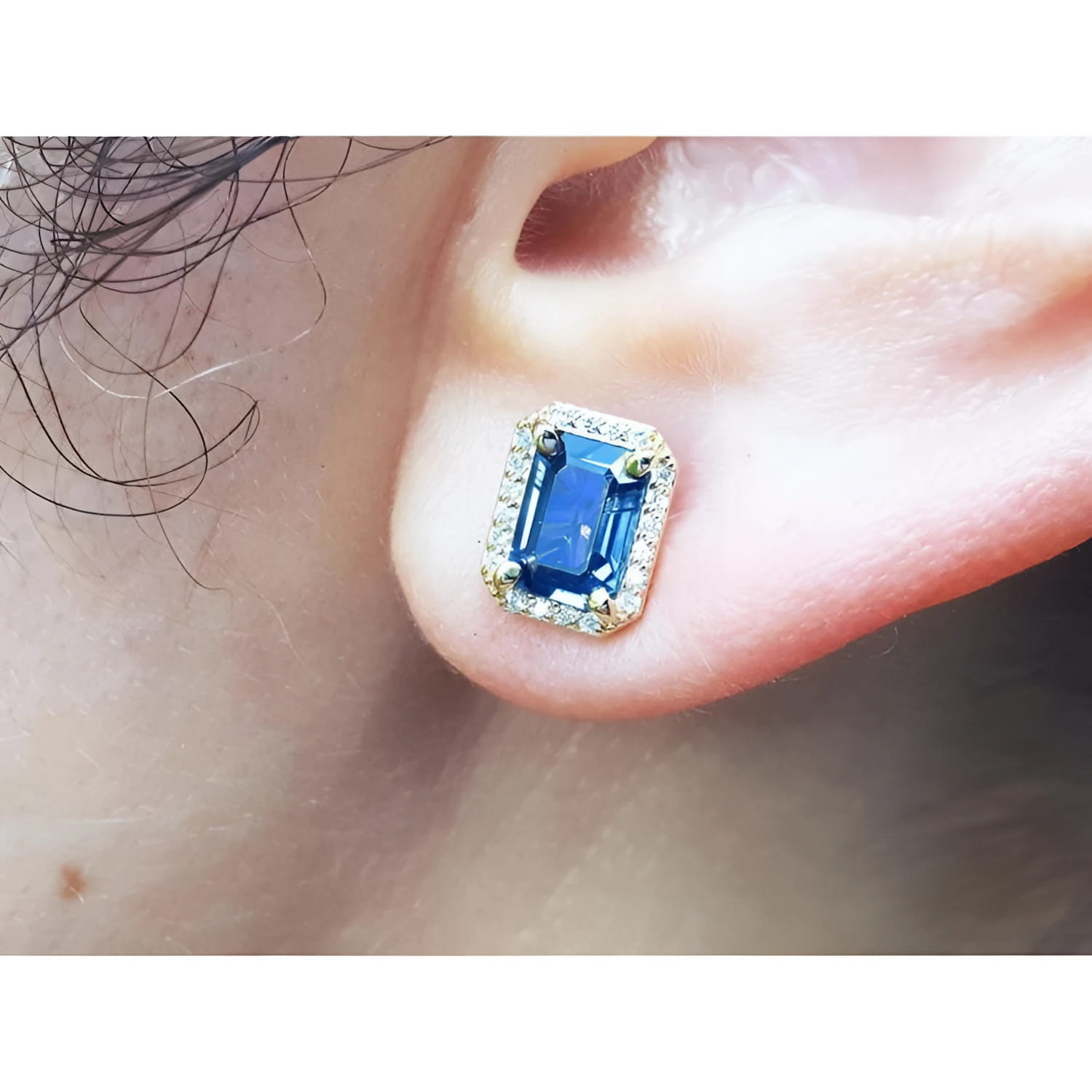 Close-up of an ear wearing a blue sapphire earring with gold setting.
