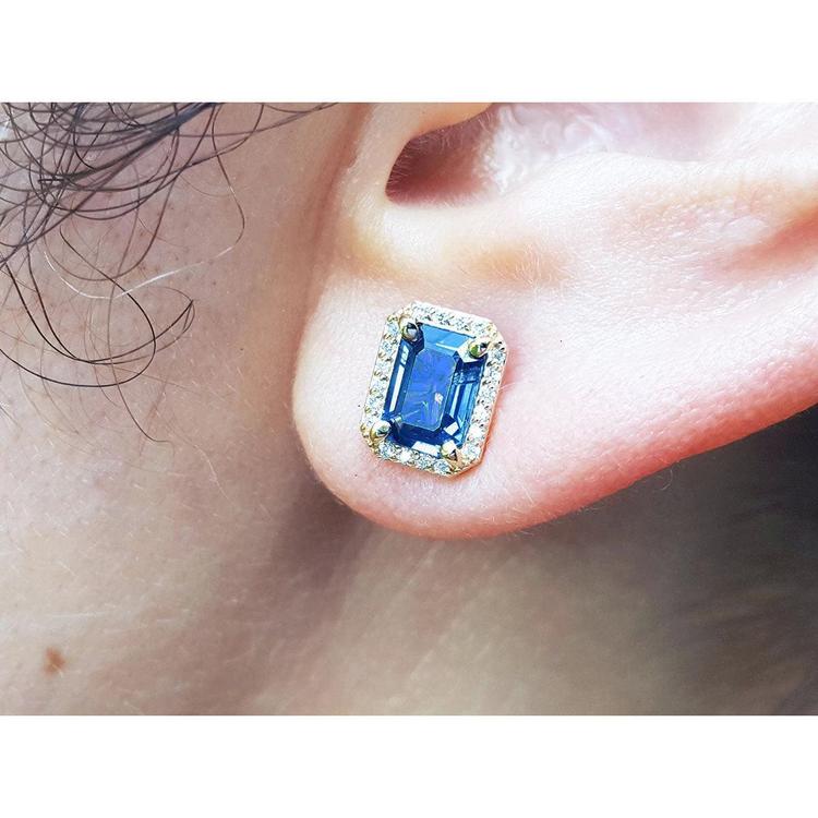 Close-up of an ear wearing a blue sapphire earring with gold setting.