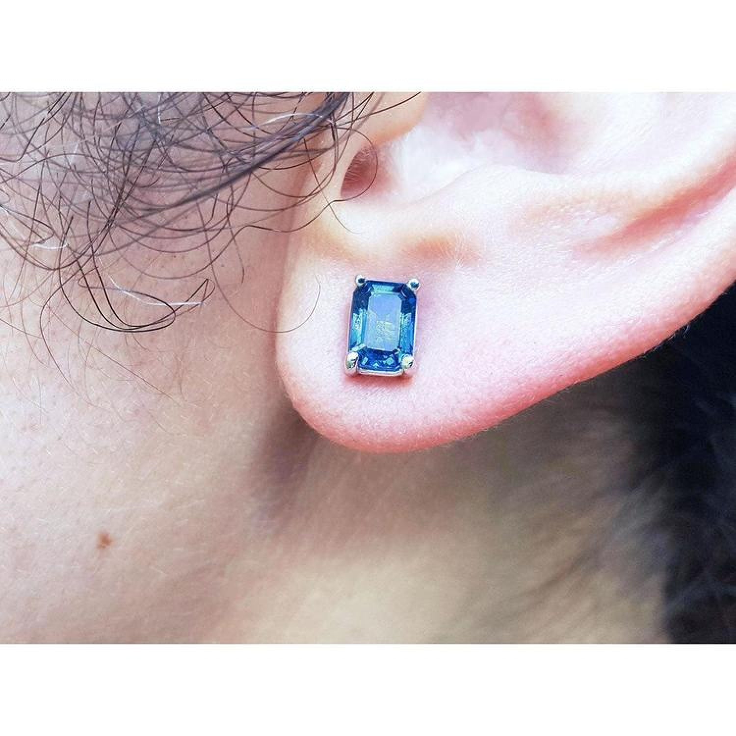 Emerald cut deep blue sapphire stud earring in 14K white gold on an ear.