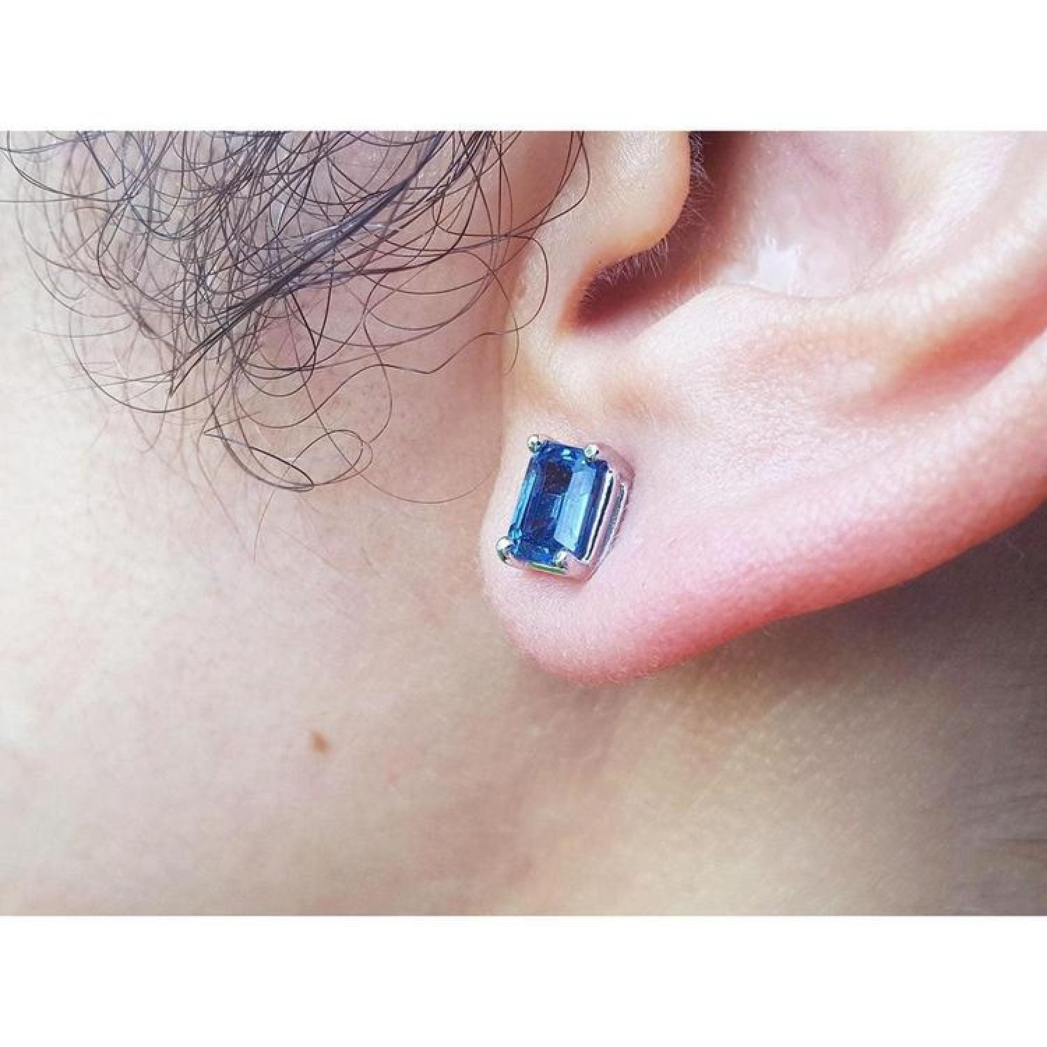 Emerald cut deep blue sapphire stud earring in 14K white gold worn on an ear.